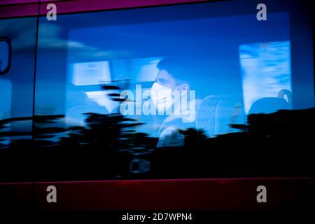 Belgrado, Serbia - 09 ottobre 2020: Persona blurry che indossa la maschera chirurgica facciale che cavalcano su un posto della finestra di un autobus di trasporto pubblico, con riflessi Foto Stock