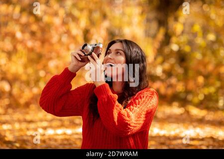 Fotografo professionista femmina che scatta foto con la fotocamera retrò all'esterno soleggiato giorno d'autunno Foto Stock