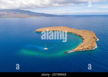 Molokini Crater, foto aerea di tutta l'isolotto a forma di mezzaluna con una barca a vela charter e l'isola di Maui sullo sfondo, Hawaii. Foto Stock