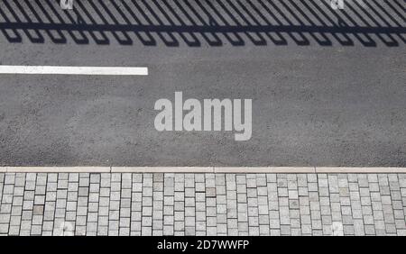 Dettaglio della strada pedonale con pista ciclabile, marciapiede pedonale e ombra di una recinzione in bianco e nero Foto Stock