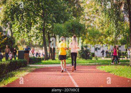 Coppia di bambini ragazzo e ragazza che fanno allenamento cardio, jogging nel parco sulla pista da jogging rosso. Simpatici gemelli che si uniscono. Correre bambini, giovani atleti. Teen Foto Stock