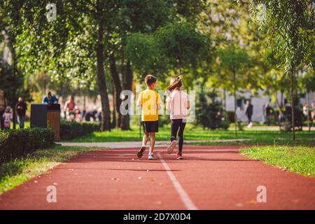 Attività ricreative e sport bambini in pre-adolescenza. Gemelli caucasici ragazzo e ragazza 10 anni jogging su pista di gomma rossa attraverso il parco. Bambini Foto Stock