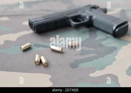 pallottole e pistola 9mm si trovano su tessuto verde camouflage. Un set di articoli della gamma di tiro o un kit di auto-difesa. Conchiglie d'oro vicino alla pistola Foto Stock