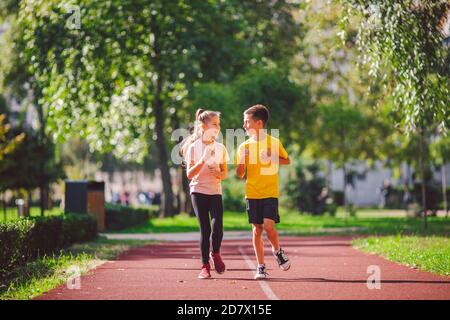 Fitness per bambini, bambini gemelli che corrono sulla pista dello stadio nel parco cittadino, allenamento e bambini che praticano uno stile di vita sano. Attività all'aperto con la corsa make Foto Stock