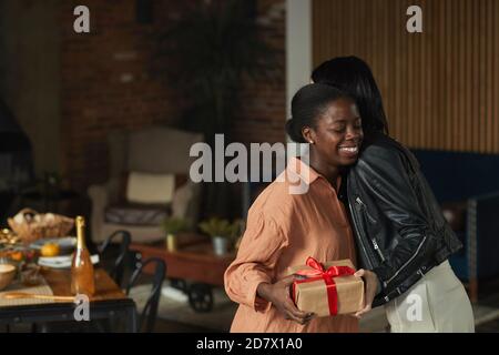 Ritratto con vista laterale di un'elegante donna afro-americana che abbatti l'amico mentre accoglie gli ospiti per la cena a casa, spazio copia Foto Stock