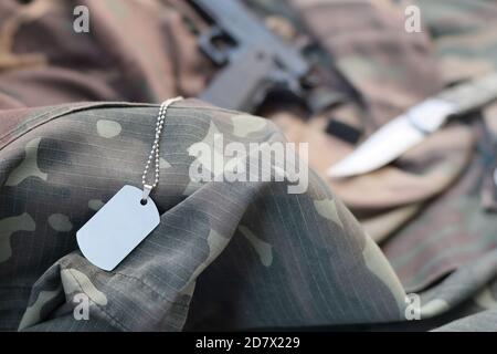 Il gettone per l'etichetta Army Dog con coltello e pistola si trova su tessuto verde mimetizzato ripiegato. Un set di articoli militari veterani o vecchio kit trofeo di dovere Foto Stock