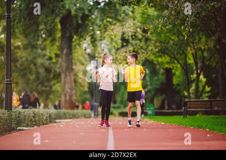 Sport e fitness in adolescenza. I gemelli caucasici, ragazzo e ragazza, corrono sulla pista da jogging nel parco cittadino. Due figli fratello e sorella per 10 anni Foto Stock