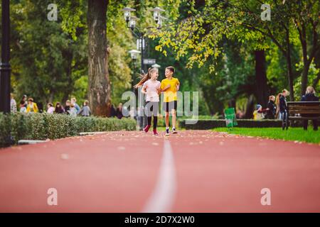 Sport e fitness in adolescenza. I gemelli caucasici, ragazzo e ragazza, corrono sulla pista da jogging nel parco cittadino. Due figli fratello e sorella per 10 anni Foto Stock