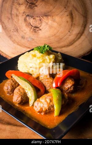 Polpette di carne in stile greco cucinate con patate, peperoni e salsa con fondo di legno Foto Stock