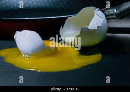 uovo rotto oltre a una padella in bassa illuminazione tasti Foto Stock