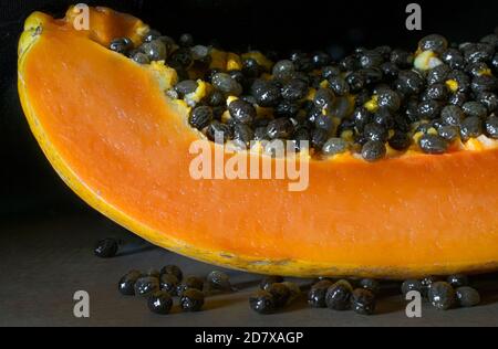 La fetta di papaya da vicino o la macrogray con i semi sopra piano con sfondo nero su un tavolo rustico Foto Stock