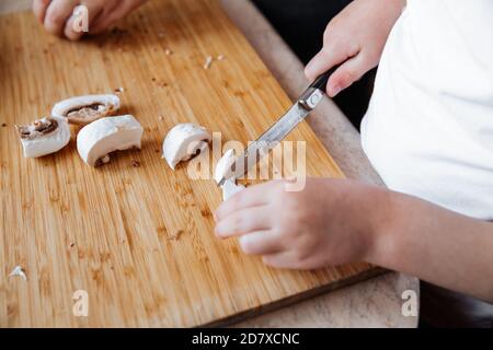 Funghi champignon freschi su tavola di legno. Una ragazza e la madre tagliarono i funghi con un coltello. Tempo trascorso insieme. Concetto di famiglia Foto Stock