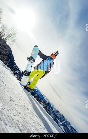 Snowboarder con brandello in maschera da sci con occhiali e un cappello mohawk in pelliccia grande sullo sfondo di un cielo e montagne innevate invernali Foto Stock