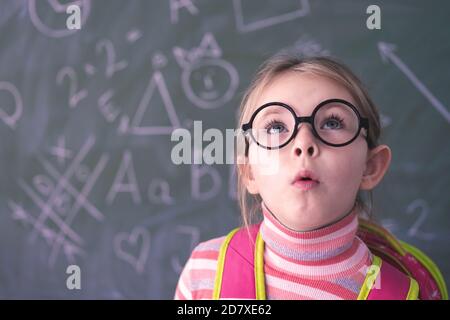 Bambina intelligente che indossa grandi occhiali mentre usa il suo computer portatile. Foto di alta qualità Foto Stock