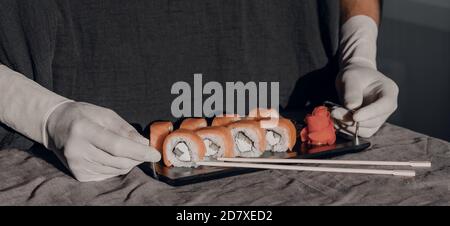 Le mani in guanti di gomma servono il sushi su un supporto nero. Menu sushi. Foto Stock
