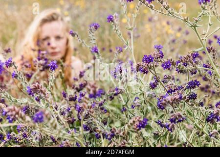 Ritratto artistico di donna frettolosa su sfondo naturale. Giovane donna che gode della natura tra i fiori e l'erba. Fuoco sui fiori Foto Stock
