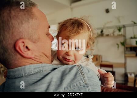 Ritratto della bambina sconvolta con la fascia che piange nei padri armi a casa Foto Stock