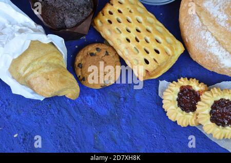 Diversi tipi di panini sulla lavagna nera dall'alto. Poster da cucina o da forno. Muffin, croissant, biscotti con patatine al cioccolato in un vasetto Foto Stock