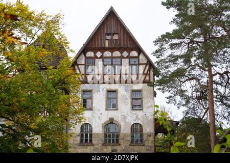 14 ottobre 2020, Brandeburgo, Lychen: Un edificio dilapido a più piani sorge tra gli alberi sul terreno del 'Parkresidenz Lychen'. Gli edifici del parco di Zenssee fanno parte dei vecchi sanatori di Hohenlychen e devono essere rinnovati e convertiti in appartamenti. Nell'ex sanatorio, il 40 per cento delle case sono già state rinnovate, ci sono appartamenti per due, quattro e sei persone, e 44 appartamenti in affitto senza barriere sono stati sviluppati e la maggior parte di loro sono già occupati. A causa del suo significato urbano, storico e architettonico, il complesso è Foto Stock