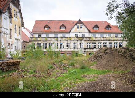 14 ottobre 2020, Brandeburgo, Lychen: Edifici a più piani derelitt si ergono dietro cumuli di terra sui terreni del 'Parkresidenz Lychen'. Le case del parco di Zenssee fanno parte dei vecchi sanatori di Hohenlychen e devono essere rinnovate e convertite in appartamenti. Nell'ex sanatorio, il 40 per cento delle case sono già state rinnovate, ci sono appartamenti per due, quattro e sei persone, e 44 appartamenti in affitto senza barriere sono stati sviluppati e la maggior parte di loro sono già occupati. A causa del suo significato urbano, storico e architettonico, il complesso è Foto Stock