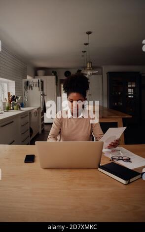 Concentrato giovane imprenditore che lavora su laptop con l'aiuto di grafico e diagrammi a casa Foto Stock