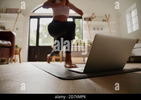 Primo piano del laptop sul tappetino fitness con la giovane donna che pratica esercizio di yoga con l'aiuto di video online Foto Stock