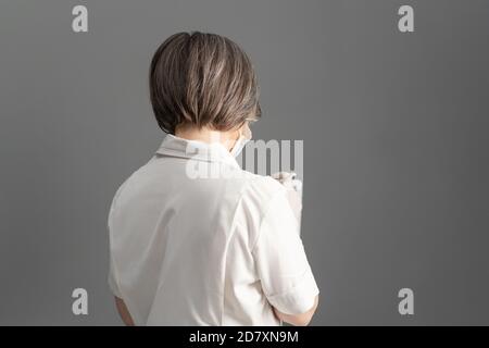 Vista posteriore della dottoressa in camice bianco con tavoletta digitale in piedi su sfondo grigio. Spazio di copia Foto Stock