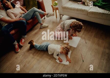 Vista ad alto angolo di due belle ragazze che si trovano sul pavimento creazione di opere su carta a casa Foto Stock