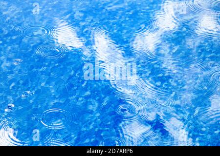 Gocce di pioggia sulla superficie blu dell'acqua della piscina. La consistenza dell'acqua blu come sfondo. Macchie circolari sull'acqua dalla pioggia Foto Stock