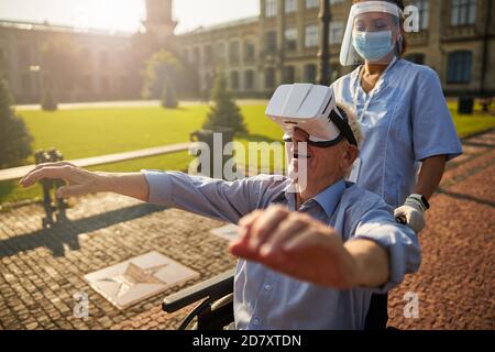 Sorridente uomo anziano che utilizza un dispositivo di realtà virtuale all'aperto Foto Stock