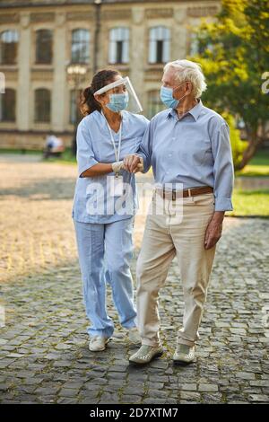 Infermiera che aiuta l'uomo anziano mentre cammina all'aperto Foto Stock