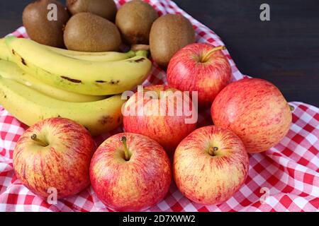 Un mucchio di mele, banane e frutta kiwi fresche mature su un panno a scacchi per il concetto di MANGIARE BENE Foto Stock