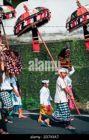 Galungan Vacanze. Un uomo e un ragazzo sono in processione festosa con ombrelli nelle loro mani. Isola di Bali, Indonesia. 26.12.2018. Foto Stock