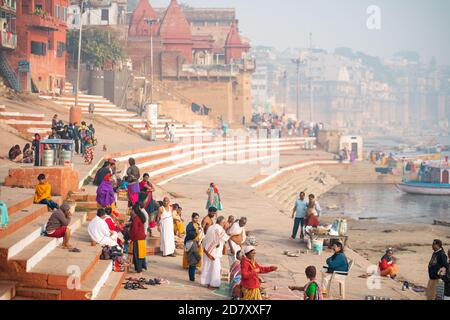 Dicembre 17 2019 Varanasi, India. La gente è occupata con i loro chores quotidiani sulle rive del fiume Gange. Gradini ed edifici sono sullo sfondo. Foto Stock