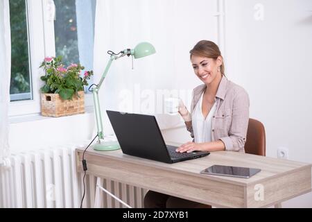 Bella giovane donna che lavora su un notebook a distanza da casa e bere il suo caffè Foto Stock