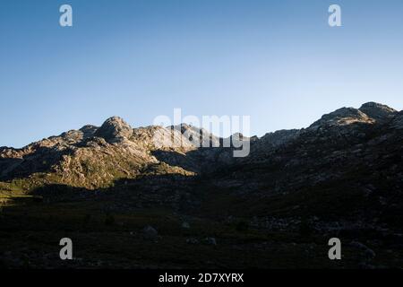 Paesaggio della valle di montagna che inizia ad essere illuminato dal primo luce al mattino mentre le ombre tornano indietro Foto Stock