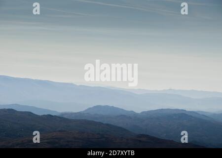 Le forme e le curve delle montagne svaniscono nell'orizzonte sottostante la nebbia mattutina Foto Stock