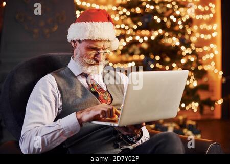 Ritratto di elegante senior con capelli grigi e barba camera di natale decorata con computer portatile in mano Foto Stock