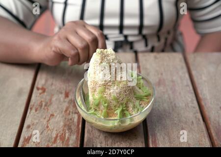 Mano della donna con cucchiaio per mangiare Cendol - un dolce ghiaccio rasato con farina di riso verde gelatina dessert. Foto Stock