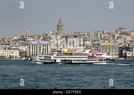 Un traghetto passeggeri naviga lungo il Corno d'Oro, che è un affluente del Bosforo a Istanbul in Turchia. Sulla collina distante si trova la Torre Galata. Foto Stock