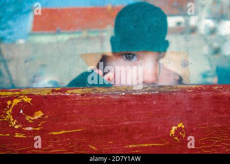 Bambino che guarda con paura attraverso una finestra Foto Stock