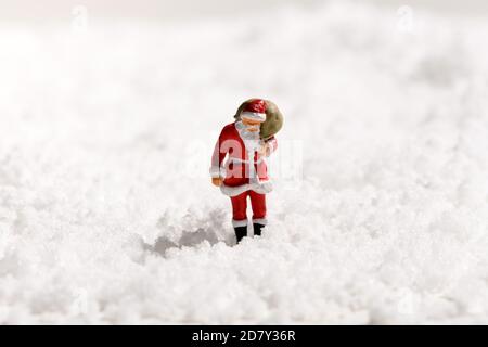 Babbo Natale in miniatura con un sacco pieno di regali a piedi attraverso neve fresca bianca invernale con spazio per la copia per il Saluto di Natale stagionale Foto Stock