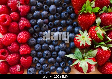 Fragola fresca, mirtillo e lampone. Frutta fresca di foresta colorata su sfondo di legno. Foto Stock