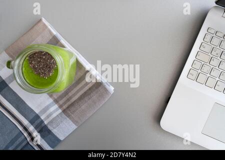 Smoothie spinaci e kiwi con laptop su sfondo grigio.spazio di lavoro sano, pausa di tempo, freelance e nomade digitale concetto. Foto Stock