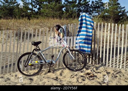 Una bicicletta accanto ad una recinzione sulla spiaggia con un asciugamano appeso alla recinzione Foto Stock