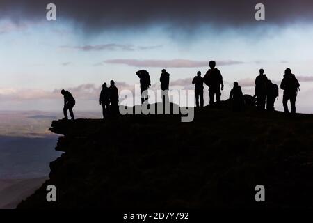 Silhouette nere di escursionisti sulla cima di una montagna che riposa sotto una nuvola grigia dopo una salita di montagna. Foto Stock