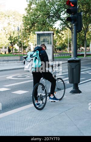 Madrid, Spagna - 3 ottobre 2020: Il pilota che effettua la consegna del cibo controlla i nuovi ordini nel suo smartphone mentre tiene in mano la sua moto. Sfondo urbano. Concetto: Food de Foto Stock