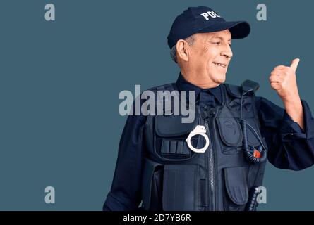 Uomo anziano bello che indossa uniforme della polizia sorridente con faccia felice guardando e puntando al lato con il pollice in su. Foto Stock