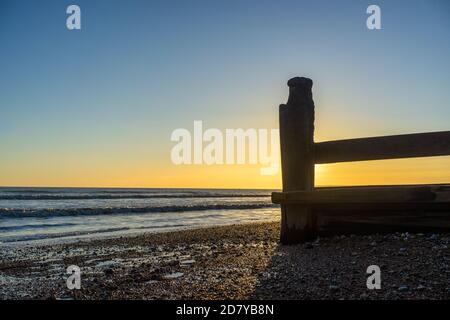 Sole che si affaccia sul mare dietro le difese di legno del mare Foto Stock