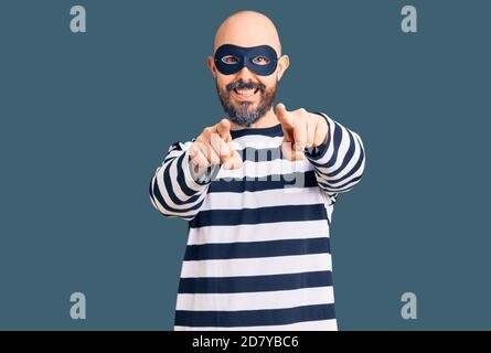 Giovane bell'uomo che indossa una maschera di scasso che punta a te e alla fotocamera con le dita, sorridendo positivo e allegro Foto Stock